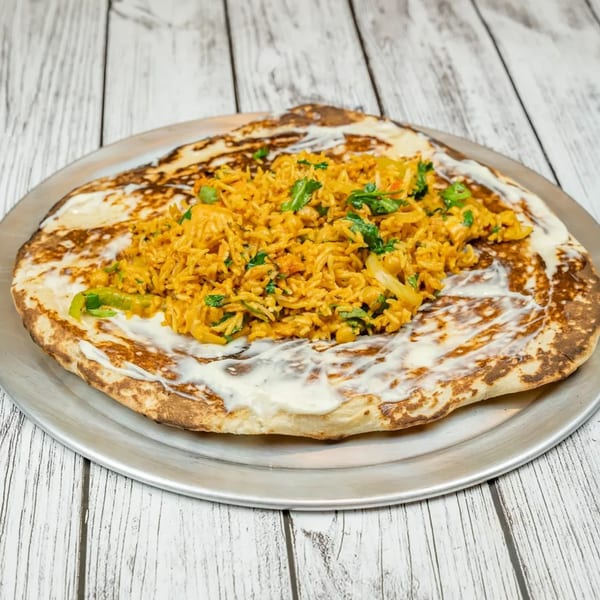 Indian flatbread topped with creamy sauce and a pile of spiced rice with green herbs.