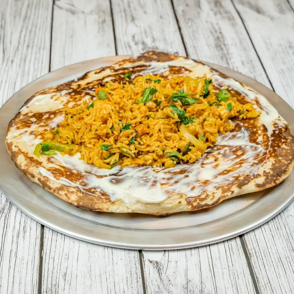 Indian flatbread topped with creamy sauce and a pile of spiced rice with green herbs.