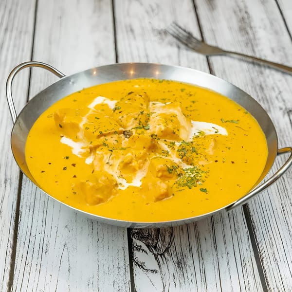 Tadka Indian Restaurant's chicken curry in a metal bowl, garnished with cream and herbs.
