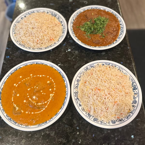 Four plates of Indian food, two with rice and two with curries, on a dark countertop.