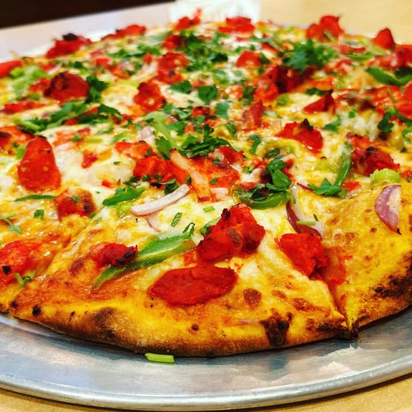 A close-up of a vibrant Indian pizza with red chicken tikka, green peppers, and cilantro.