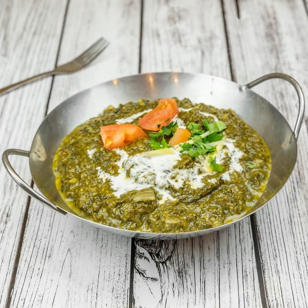 Tadka Indian Restaurant's Palak Paneer, a green spinach curry with cream, tomatoes, and cilantro in a metal bowl.