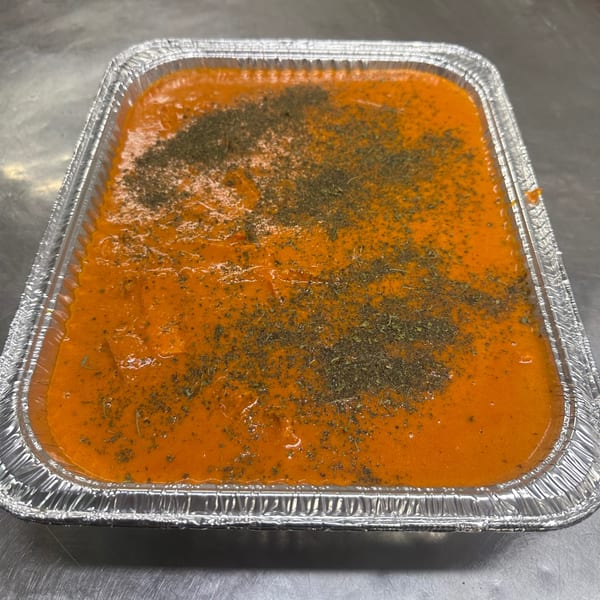 A foil tray filled with orange Indian curry, topped with dried green herbs.