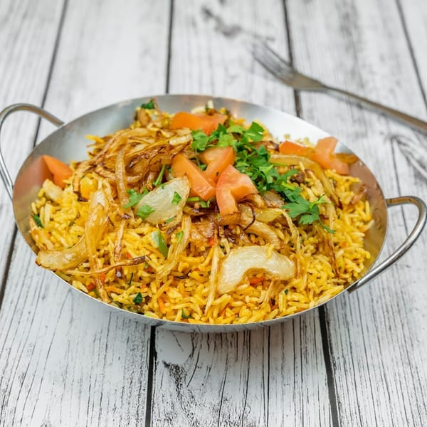 Tadka Indian Restaurant's biryani, garnished with fried onions, tomatoes, and cilantro, in a metal serving dish.